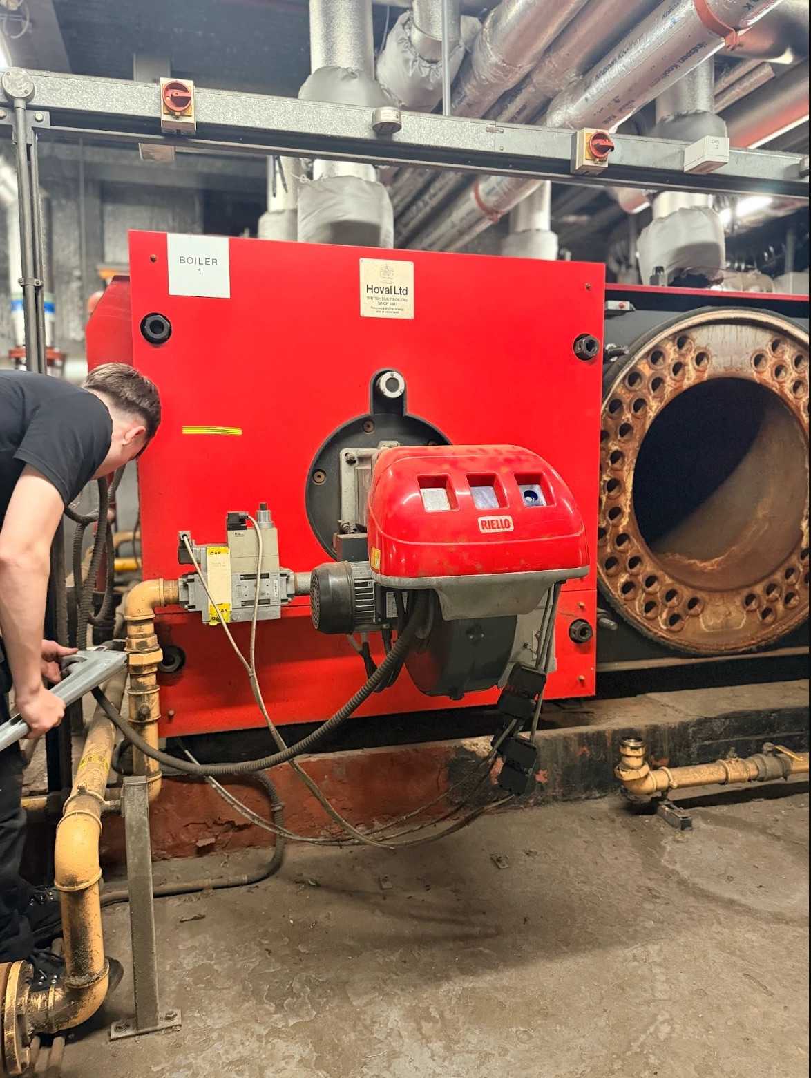 A Neos Engineering engineer working on the gas pipework of a Hoval commercial boiler with a Riello burner in a London plant room