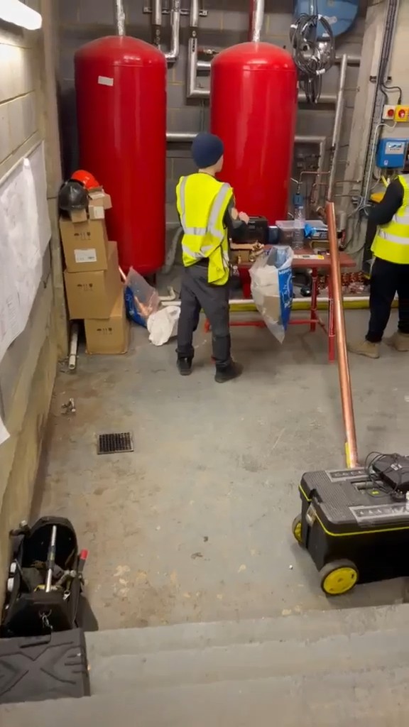 Neos Engineering engineers at a workbench beside two red pressure vessels in a commercial plant room in London